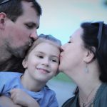 A heartwarming capture of parents showing love to their smiling daughter with gentle kisses.
