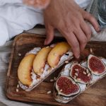 Close-up of artisan toast with fig and peach slices on a wooden tray, styled indoors.