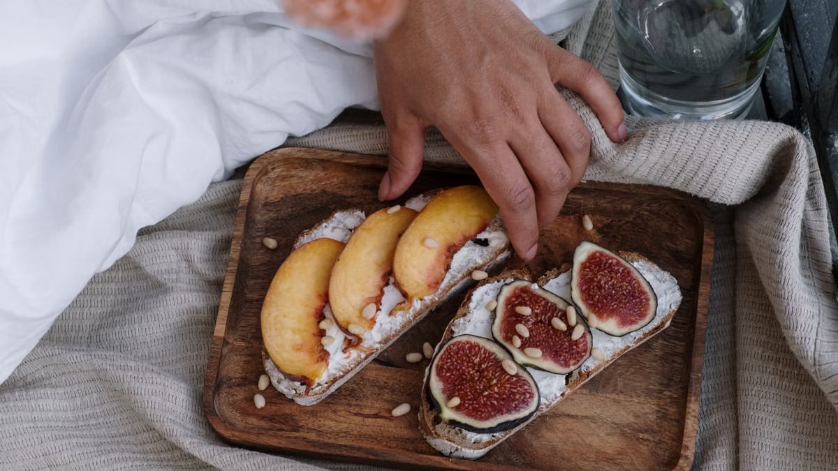 Close-up of artisan toast with fig and peach slices on a wooden tray, styled indoors.